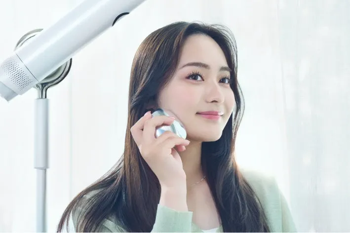 ドライヤーを使いながら美顔器でスキンケアをする女性