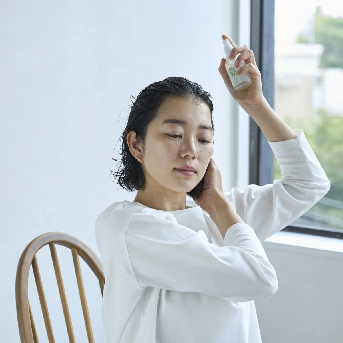鏡の前で頭皮に美容液をスプレーする女性の様子